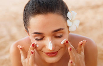 woman with flower behind her ear smears her face with sunscreen