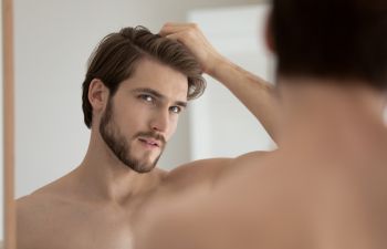 Handsome youngish looking man examining his face in a mirror.